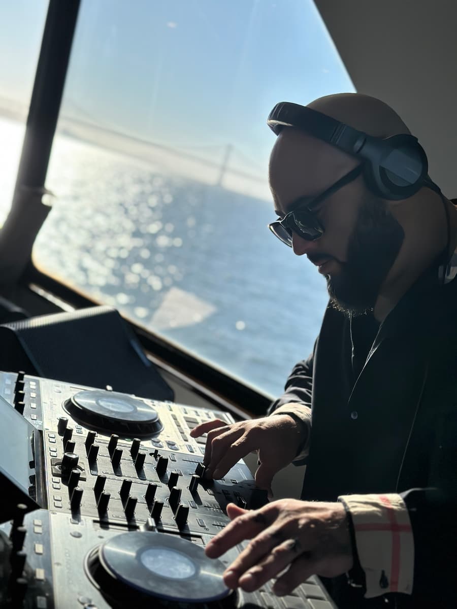 Marcus mixing at a window with the Bay Bridge and the bay glowing behind him
